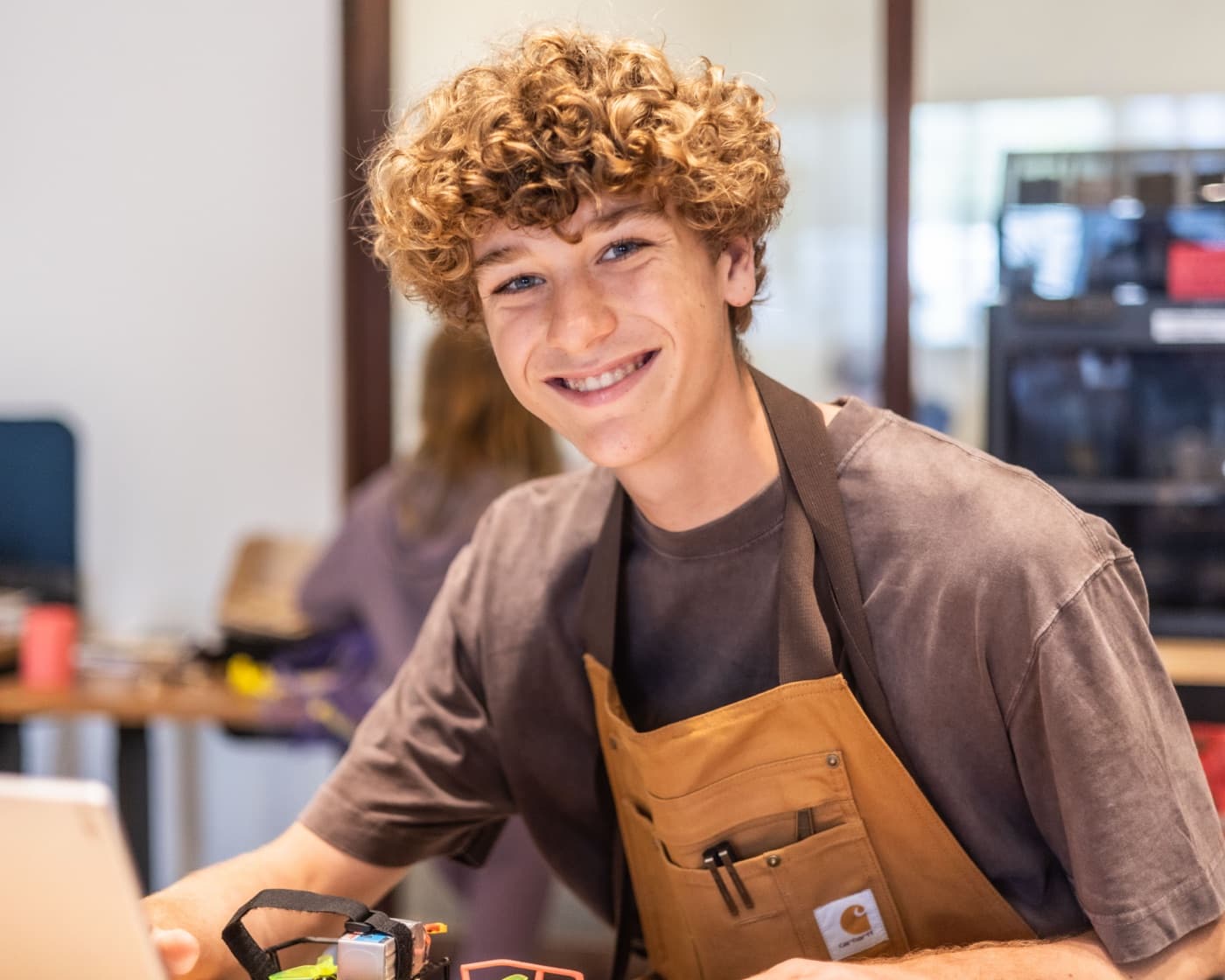 An older Forge student in a workshop apron, ready to mentor younger kids.