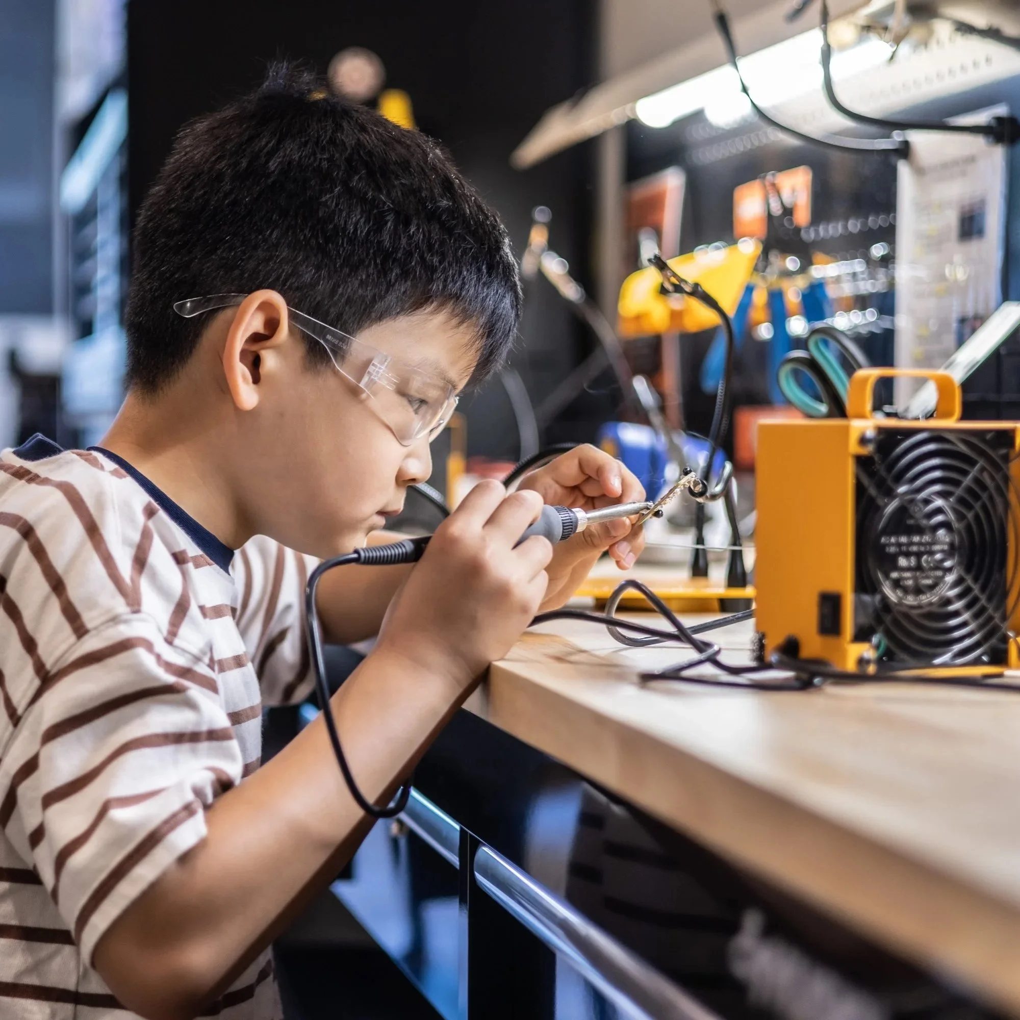 A Forge Academy student soldering at the workshop bench.