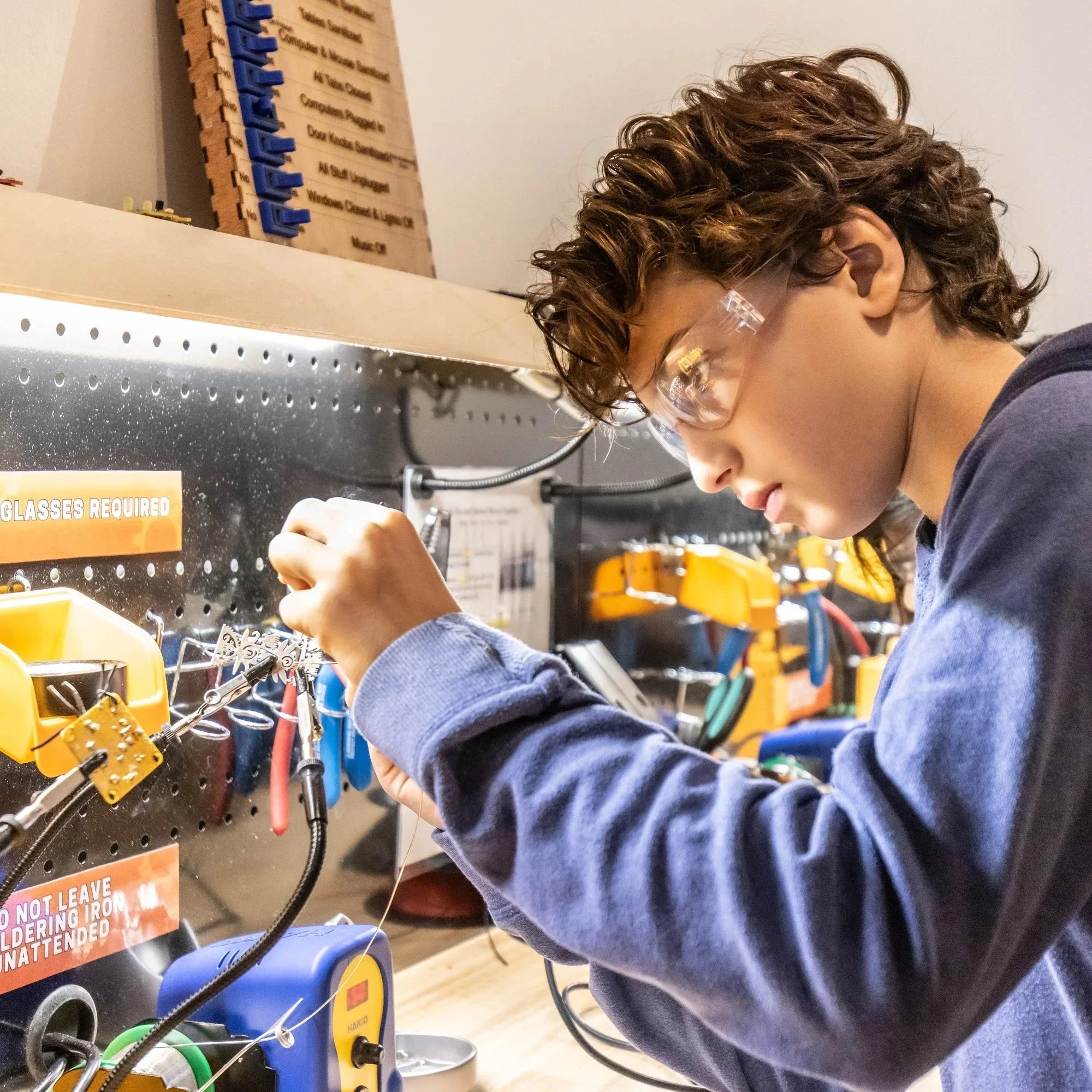 A camper soldering a project at the Forge workshop bench.
